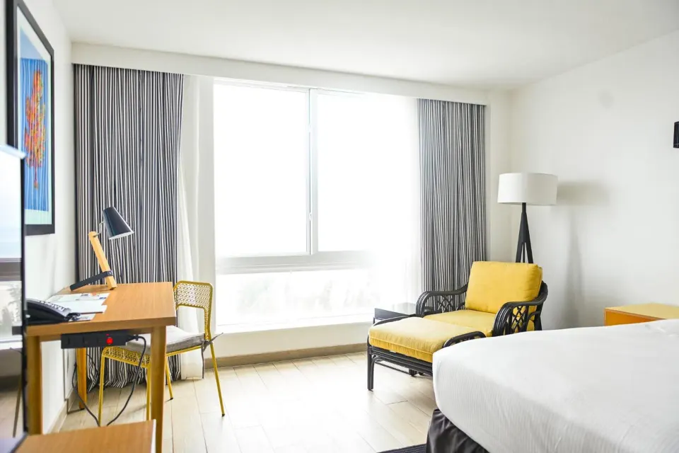 Water View room with bed, desk, yellow chair and bright window at Warwick Paradise Island.