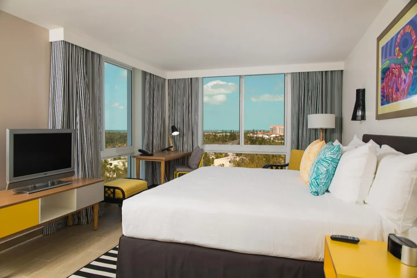 Water View king room with corner windows, bed, TV and desk at Warwick Paradise Island.
