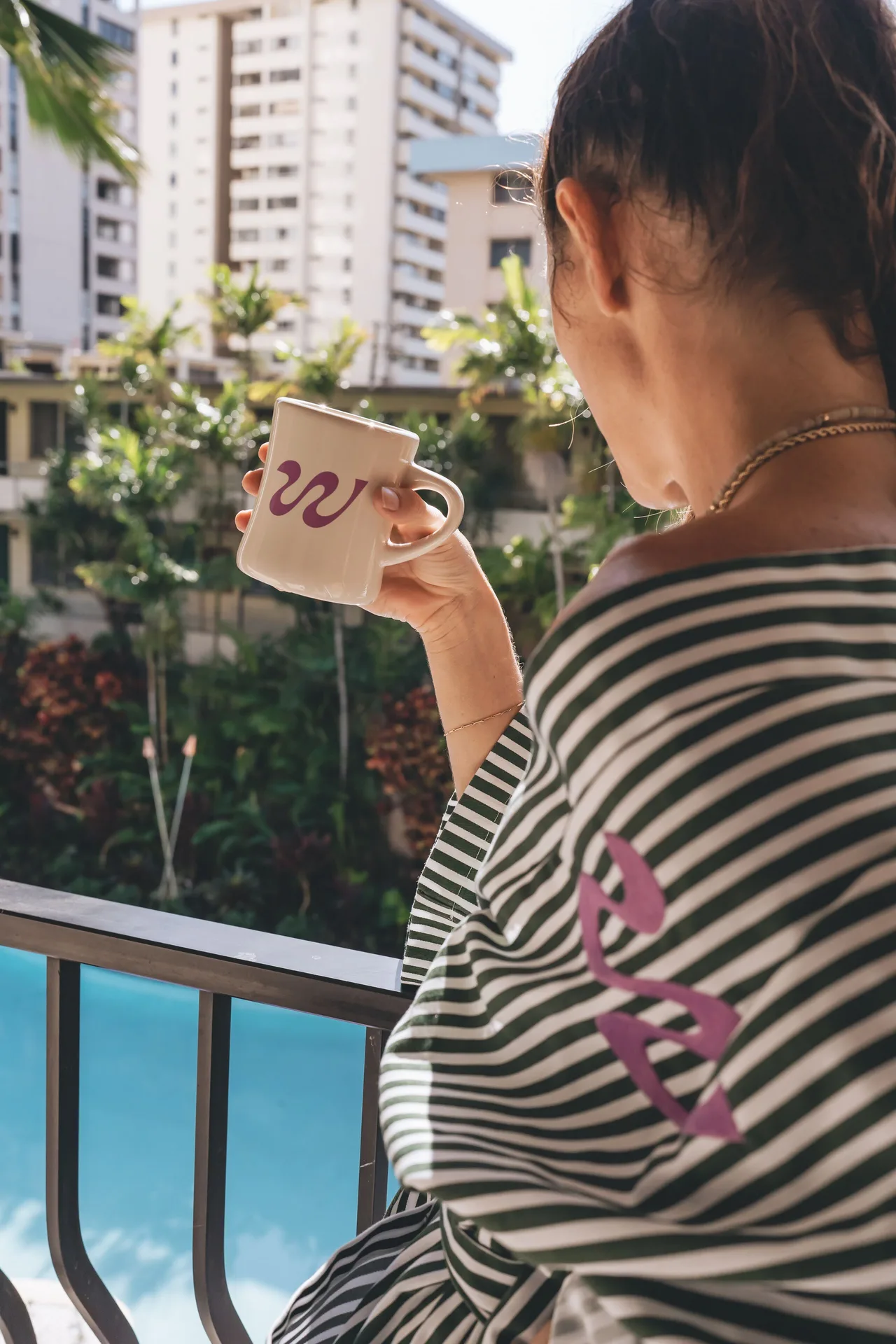Guest sipping from a mug on a balcony above the pool at Wayfinder Waikiki.