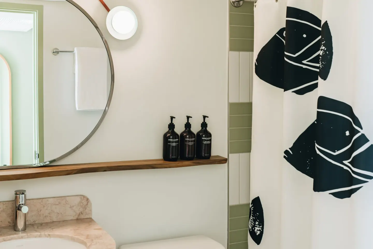 Guest bathroom vanity, round mirror, and patterned shower curtain at Wayfinder Waikiki.