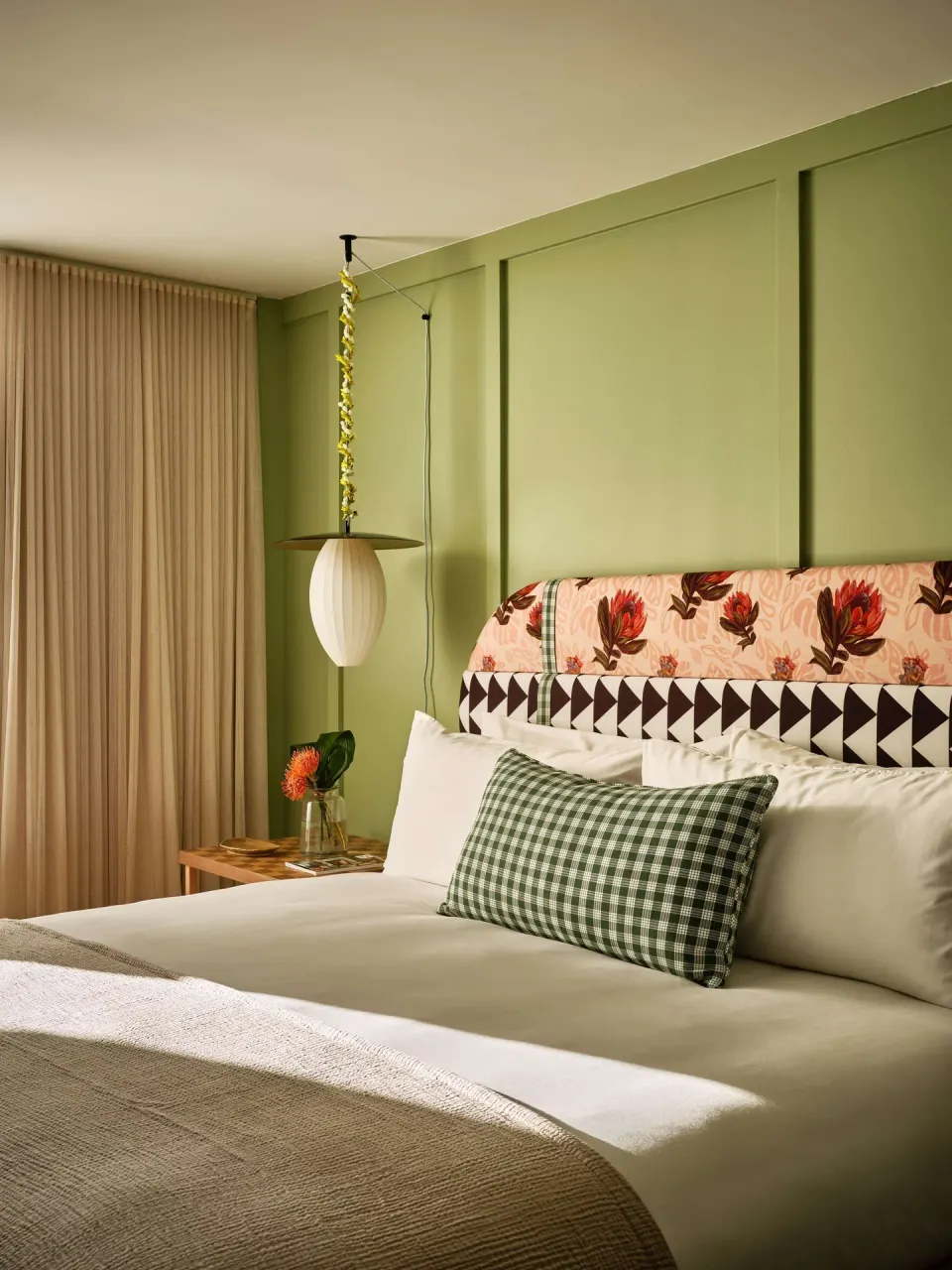 Guest room bed with floral headboard and pendant light at Wayfinder Waikiki.