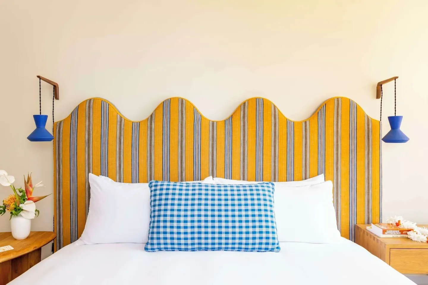 Guest room bed with striped headboard and blue lamps at Wayfinder Waikiki.