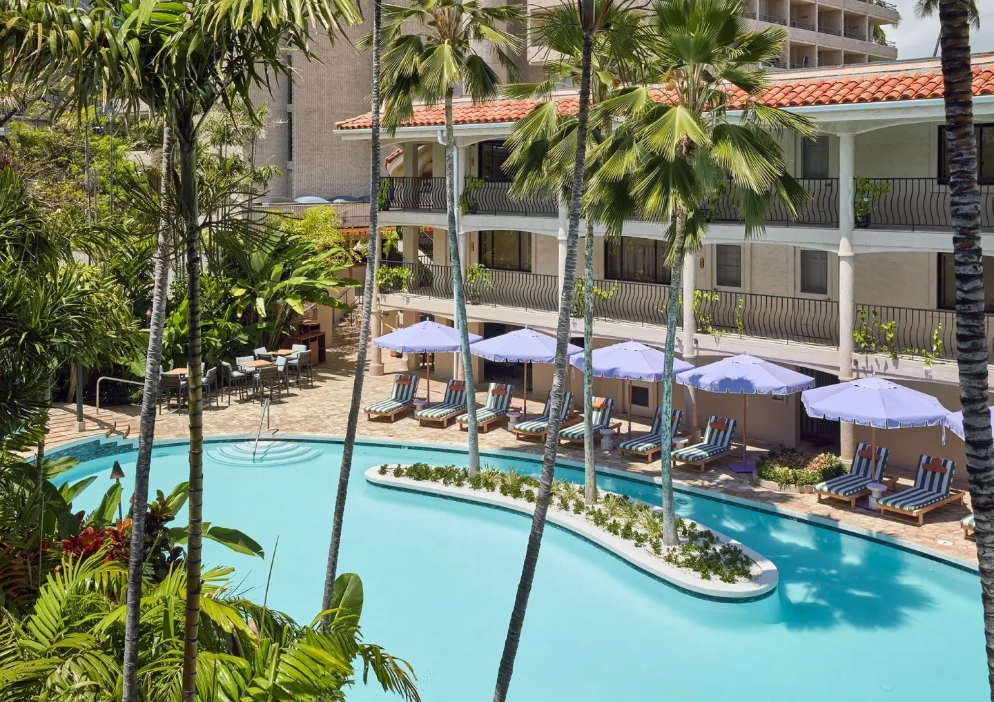 Pool courtyard with palms, loungers, umbrellas, and guest balconies at Wayfinder Waikiki.