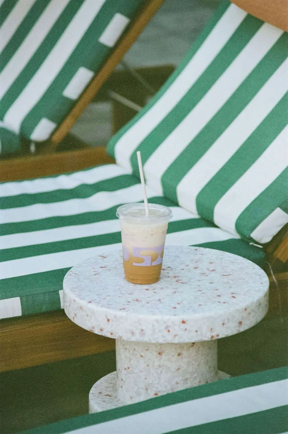 Iced drink on a white side table between green striped loungers at Wayfinder Waikiki.