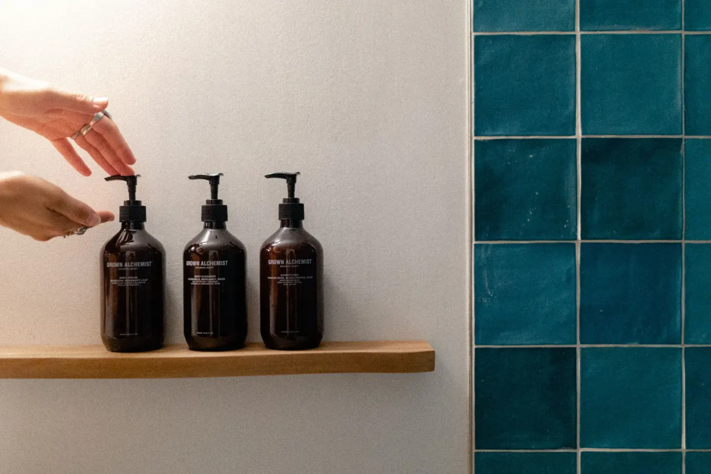 Pump-bottle bath amenities sit on a shower shelf beside teal tile at Wayfinder Waikiki.