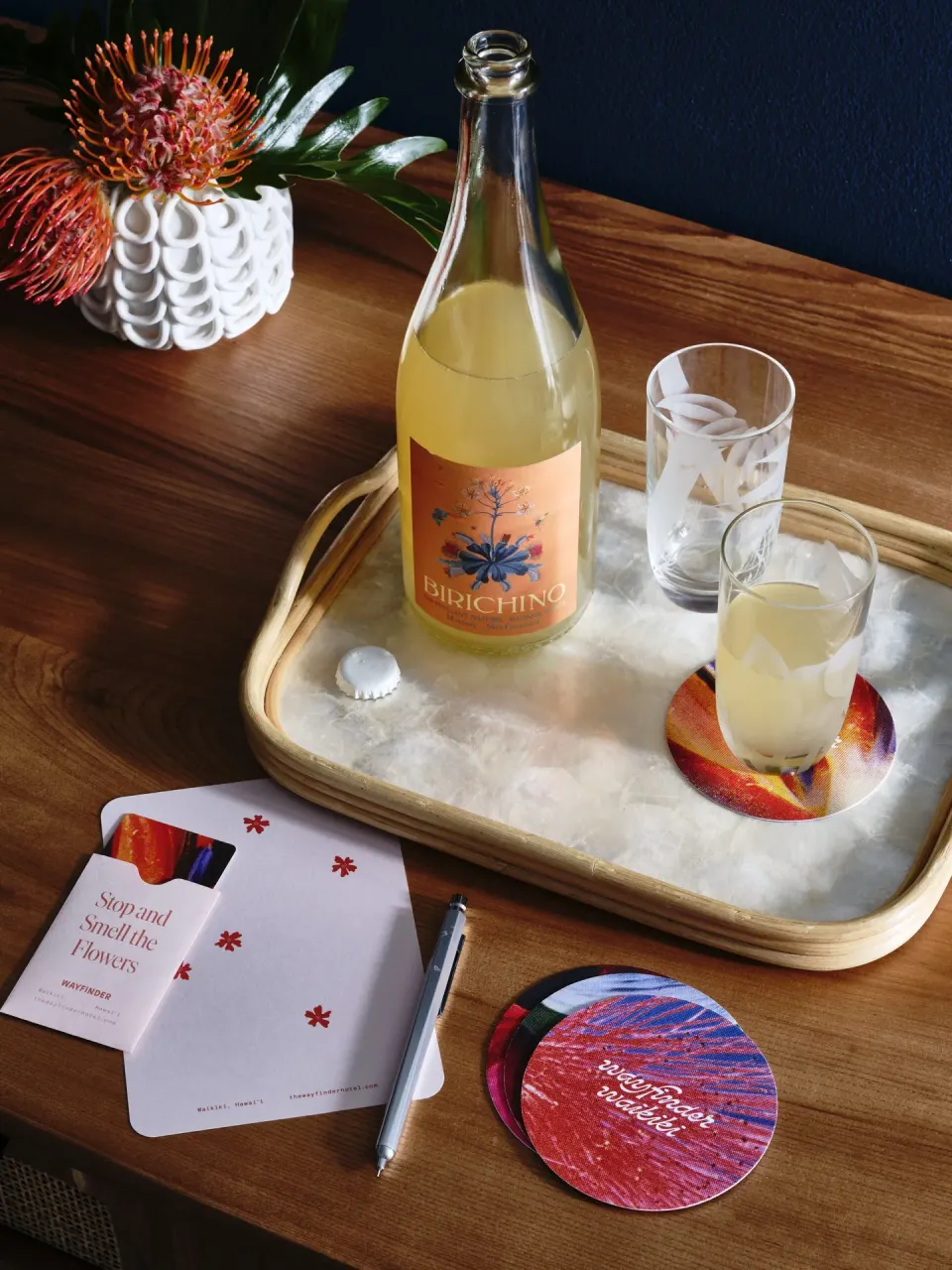 Welcome drink setup with bottle, glasses, and flowers at Wayfinder Waikiki.