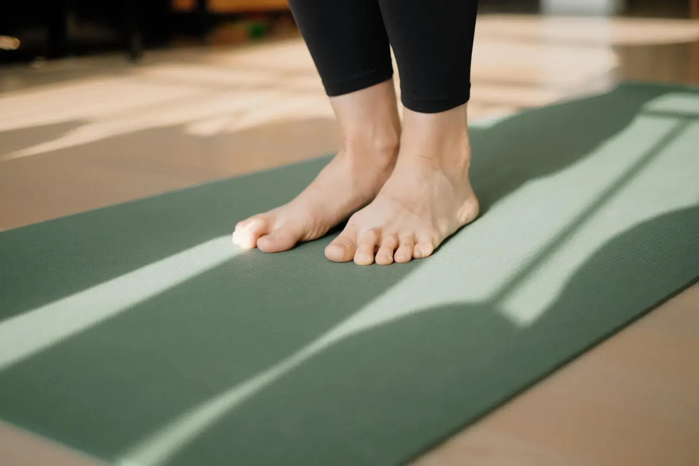 Bare feet stand on a green yoga mat in soft light at Wayfinder Waikiki.