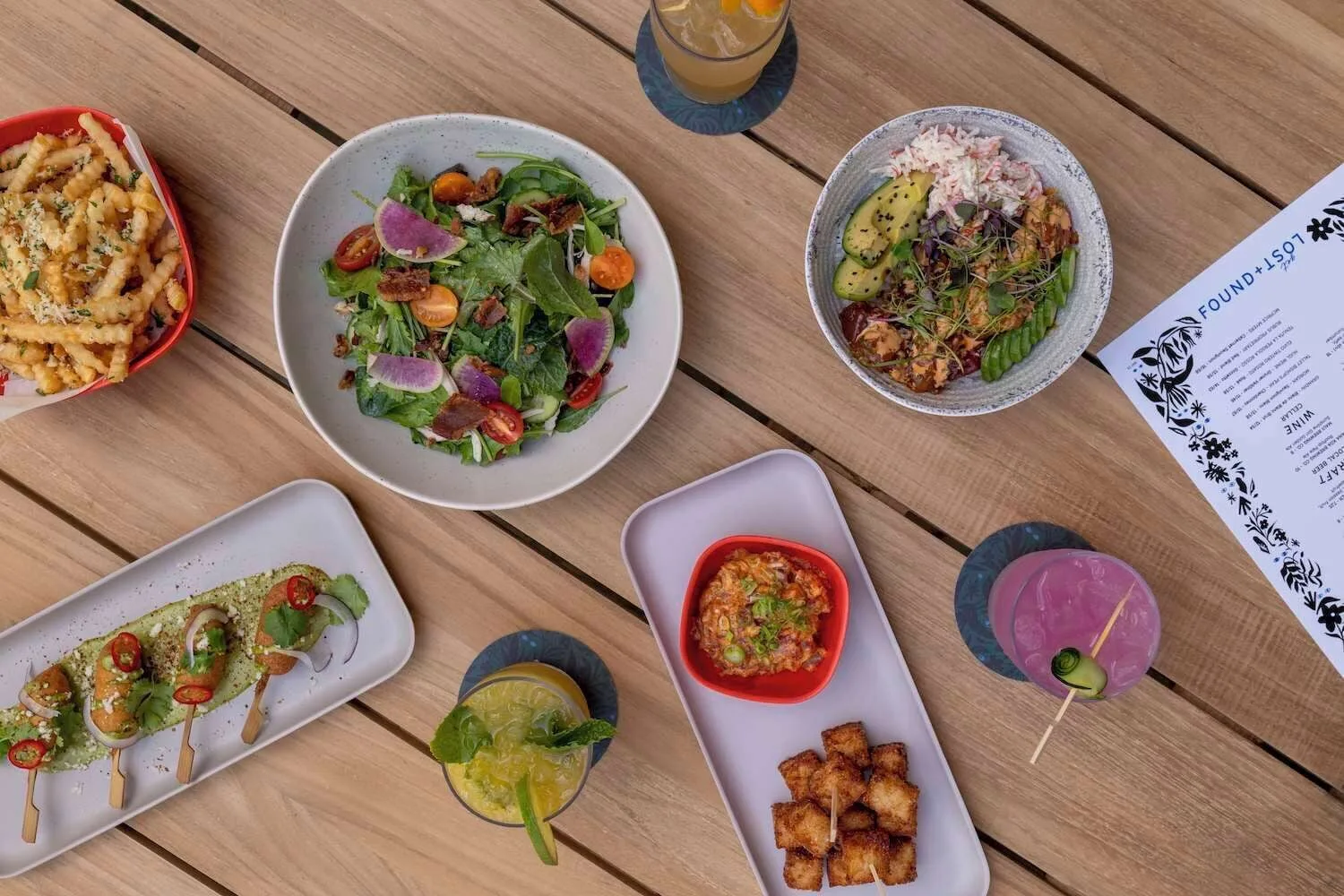 Overhead spread of plates and cocktails on a wood table at Wayfinder Waikiki.