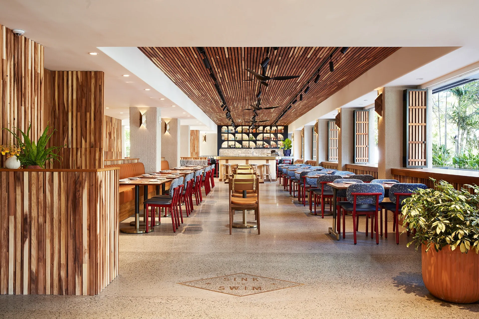 Bright dining room with red chairs and a long bar at Wayfinder Waikiki.