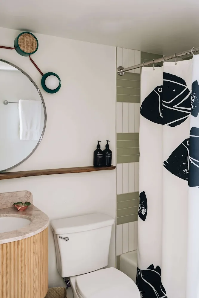 Lanai Corner bathroom with vanity, mirror and fish-print shower curtain at Wayfinder Waikiki.