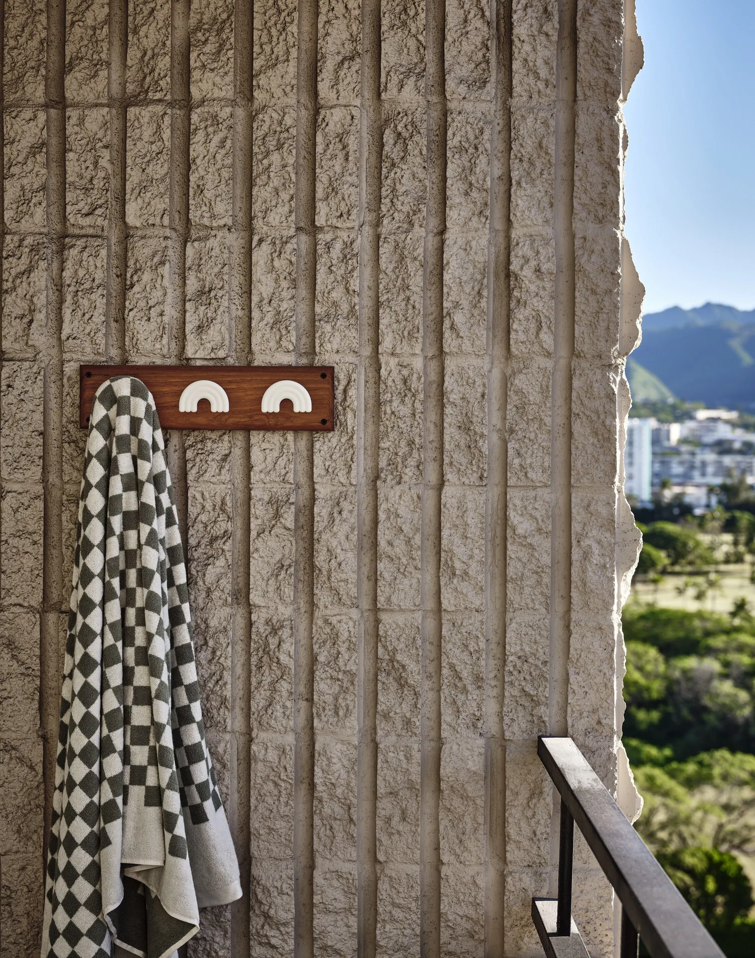 Lanai wall with hanging checkered towel and city-mountain view at Wayfinder Waikiki.