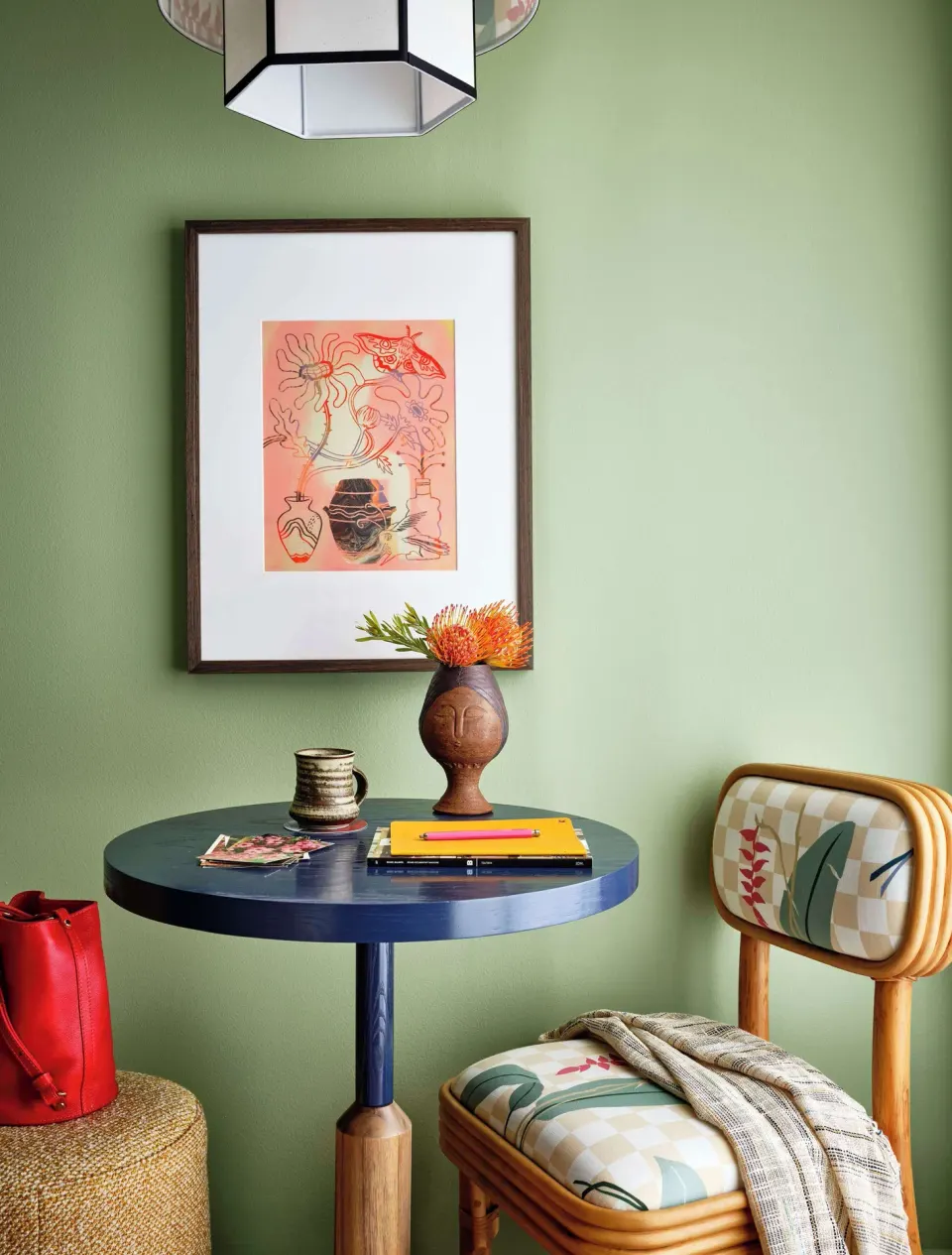 Corner room table with chair, framed art, flowers, and green wall at Wayfinder Waikiki.