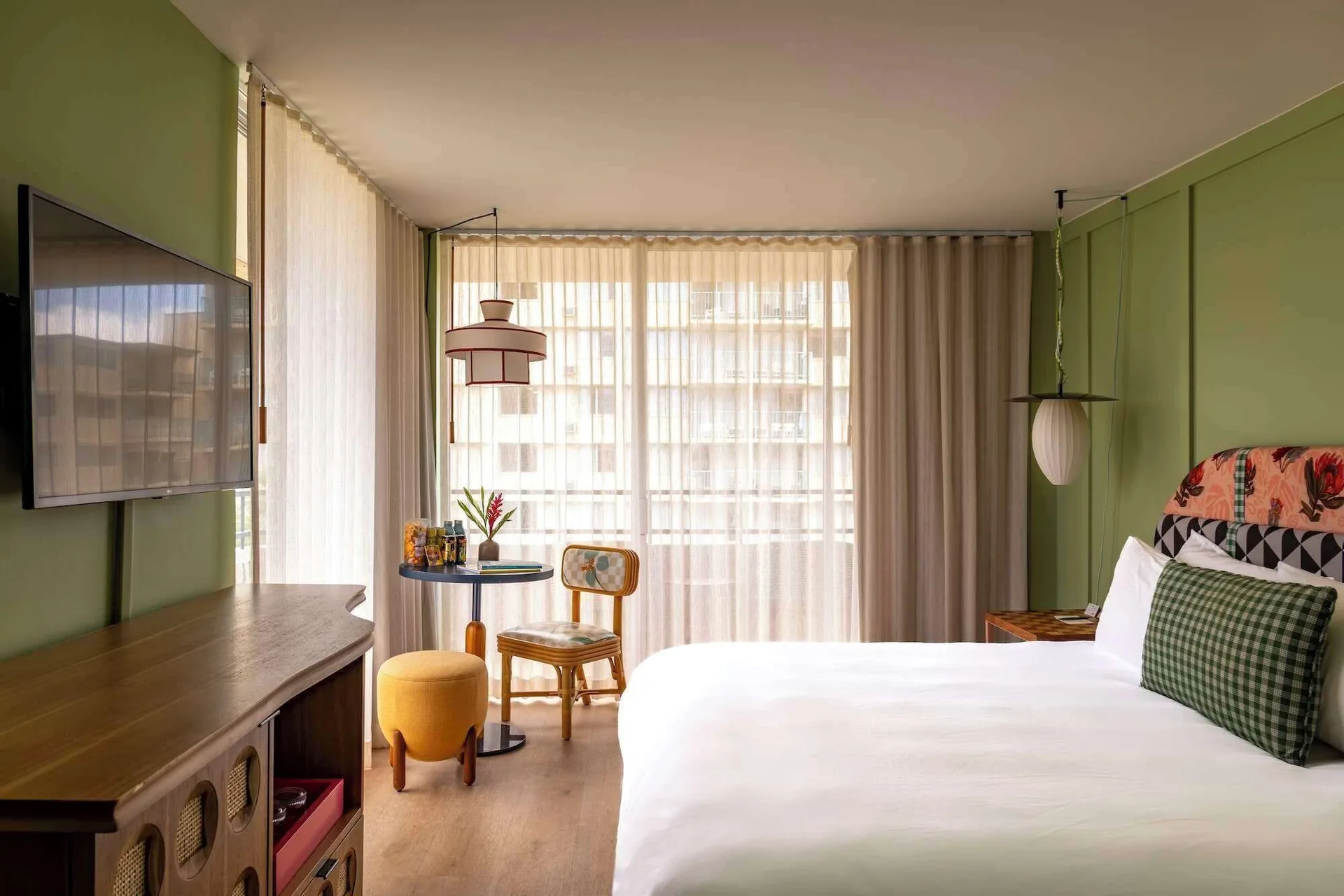 Corner guest room with king bed, TV, seating nook, and sheer lanai curtains at Wayfinder Waikiki.