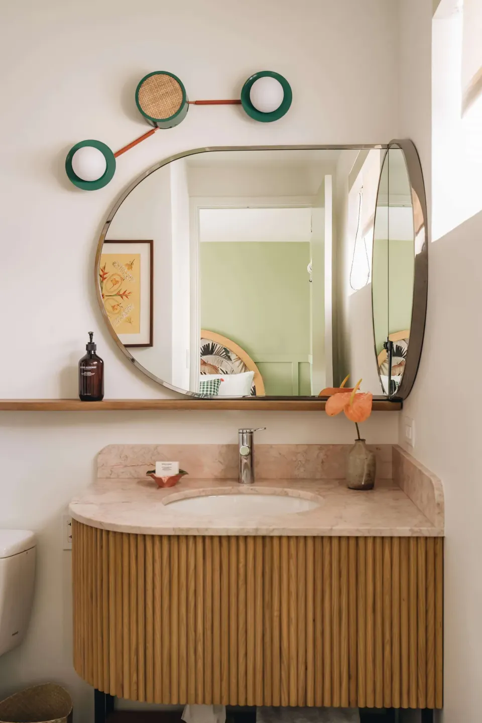 Studio bathroom vanity with round mirror, marble counter, and green accent lighting at Wayfinder Waikiki.