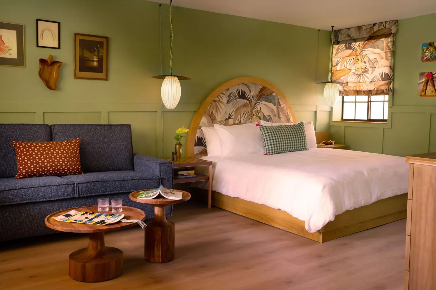Studio room with bed, sofa, green walls, and tropical window shade at Wayfinder Waikiki.