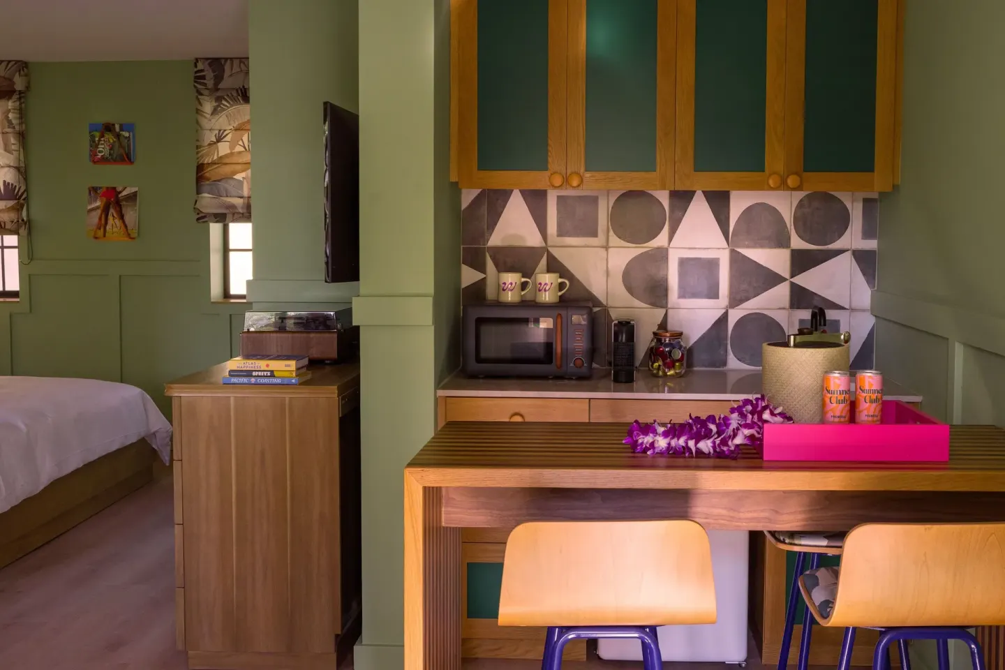 Studio kitchenette with bar stools, microwave, patterned tile, and bedroom beyond at Wayfinder Waikiki.