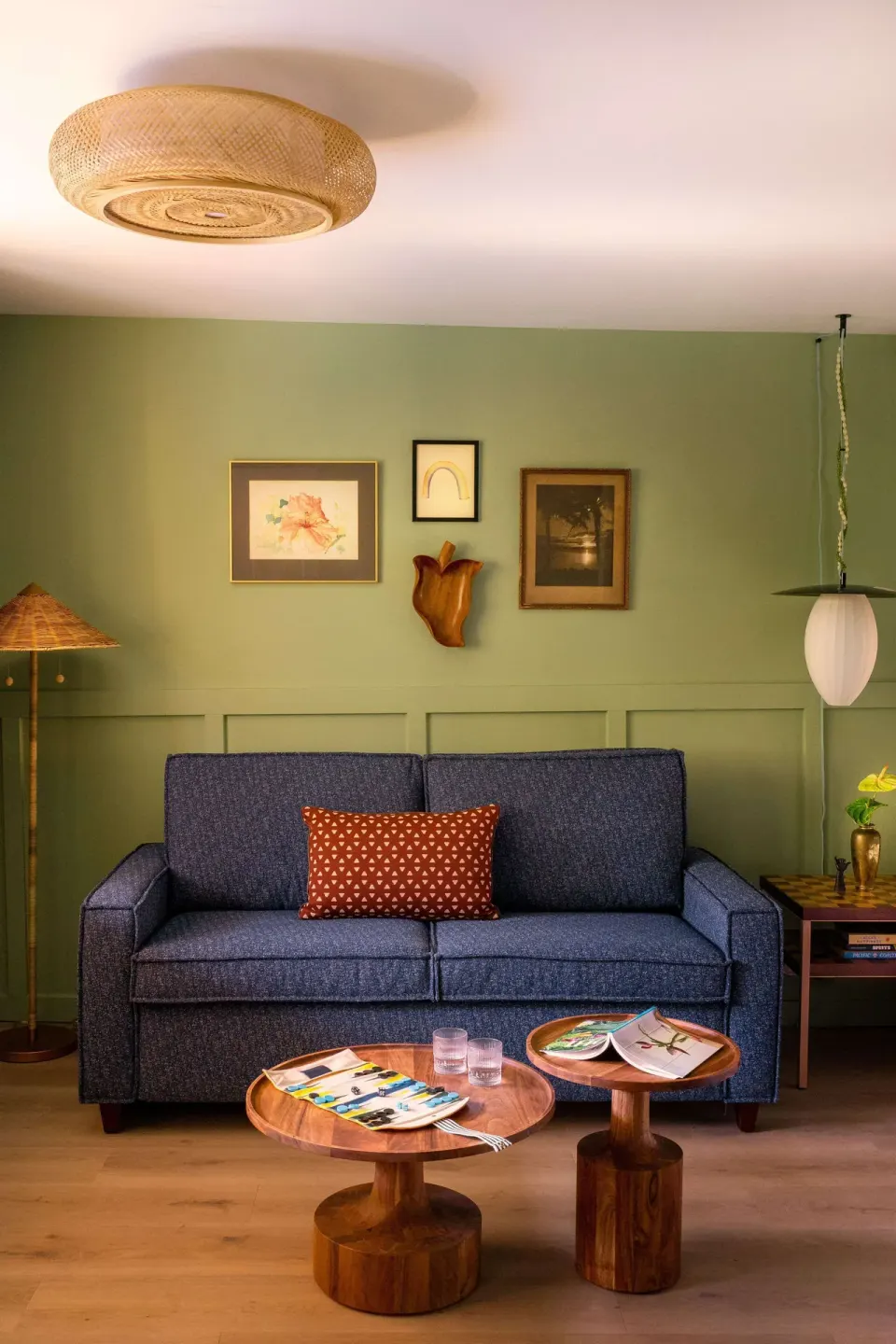 Studio seating area with blue sofa, wood tables, wall art, and pendant light at Wayfinder Waikiki.