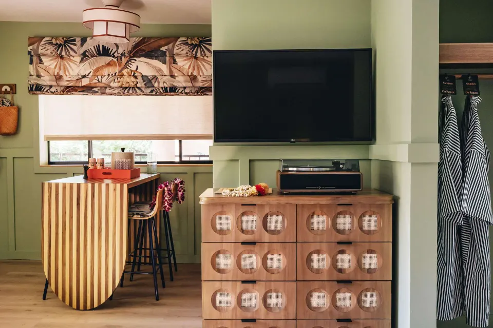 Studio room with TV, dresser, bar counter, stools, window, and striped robes at Wayfinder Waikiki.