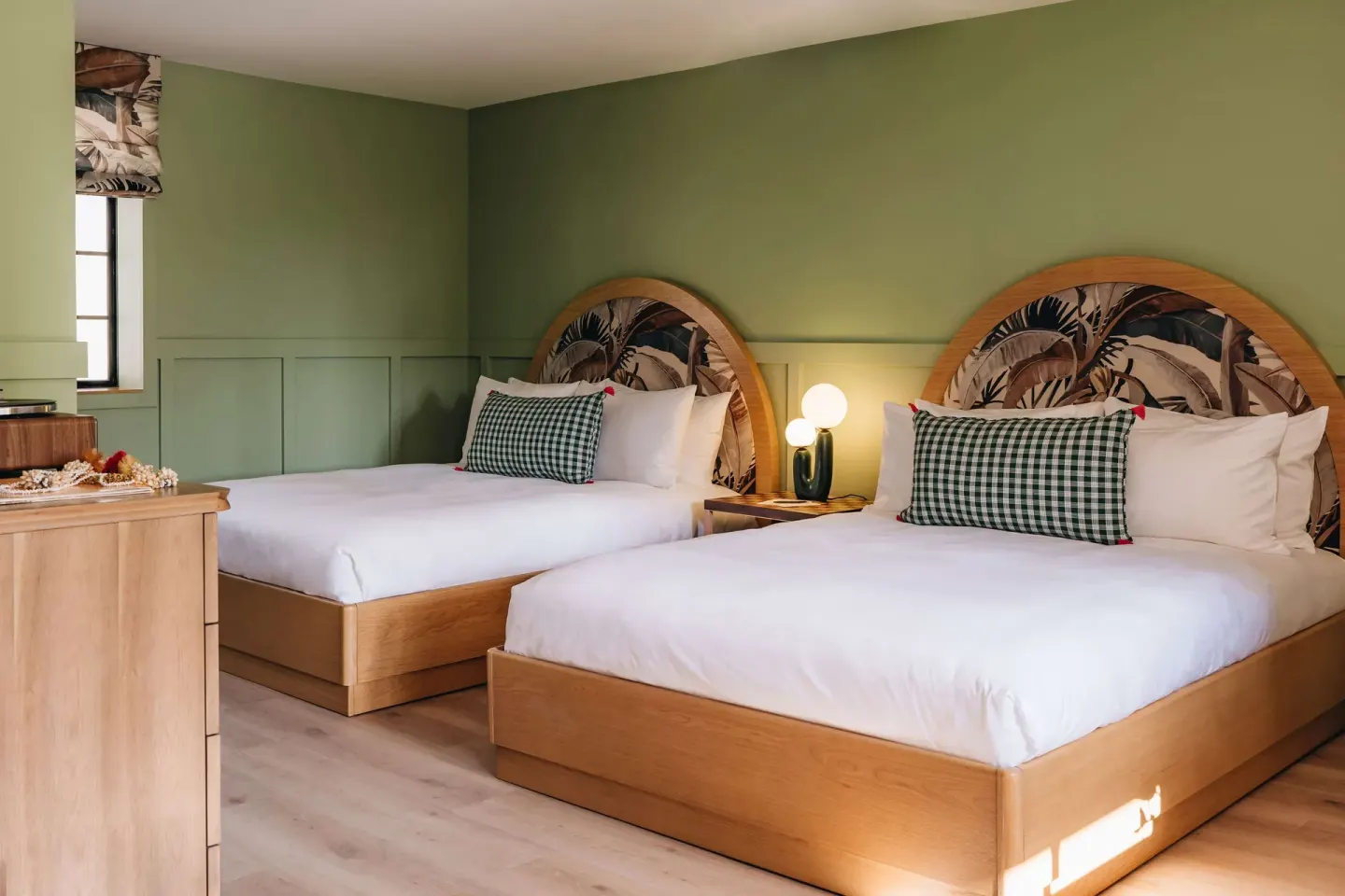 Studio room with two beds, green walls, wood furniture, and tropical headboards at Wayfinder Waikiki.