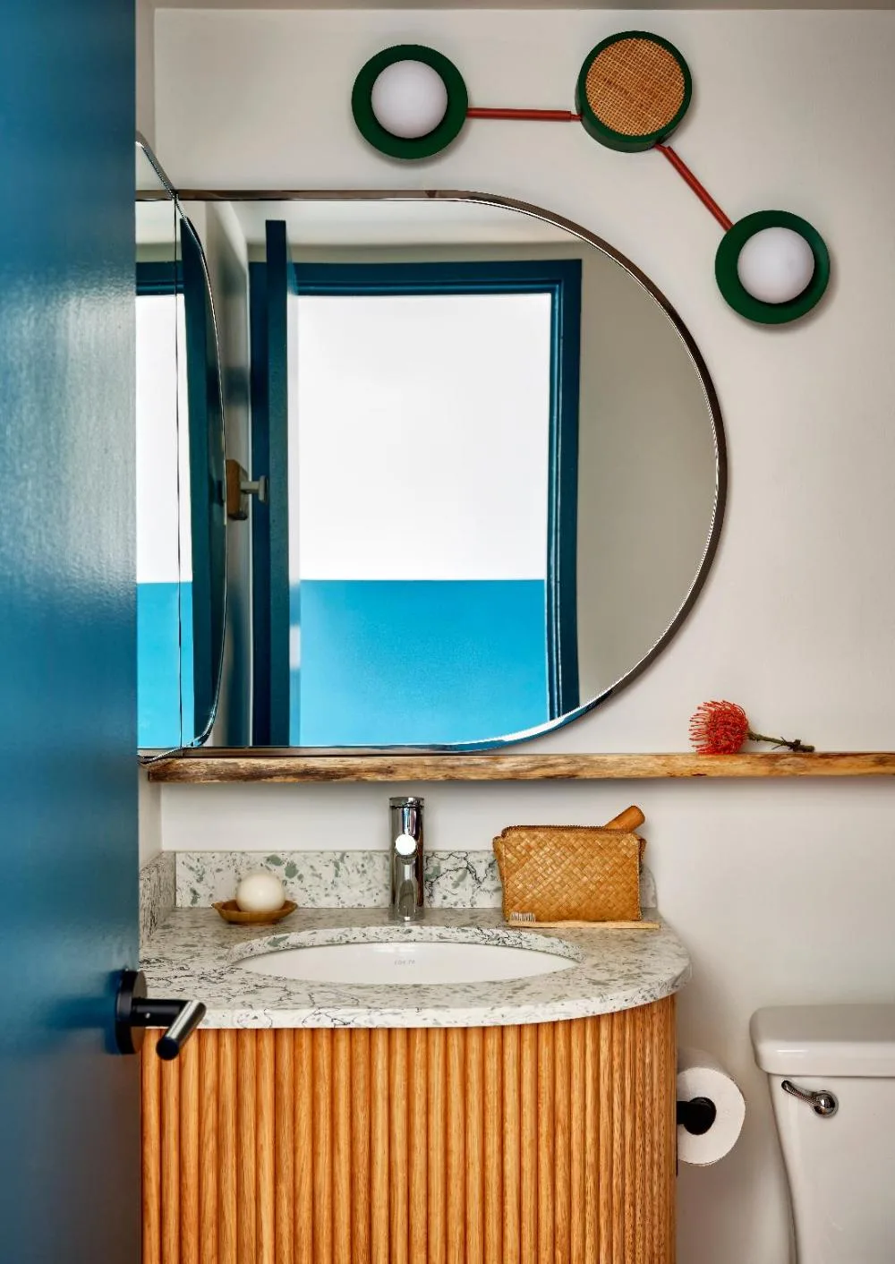 Bathroom vanity in a Two Beds with Lanai room at Wayfinder Waikiki with round mirror and wood-front sink.