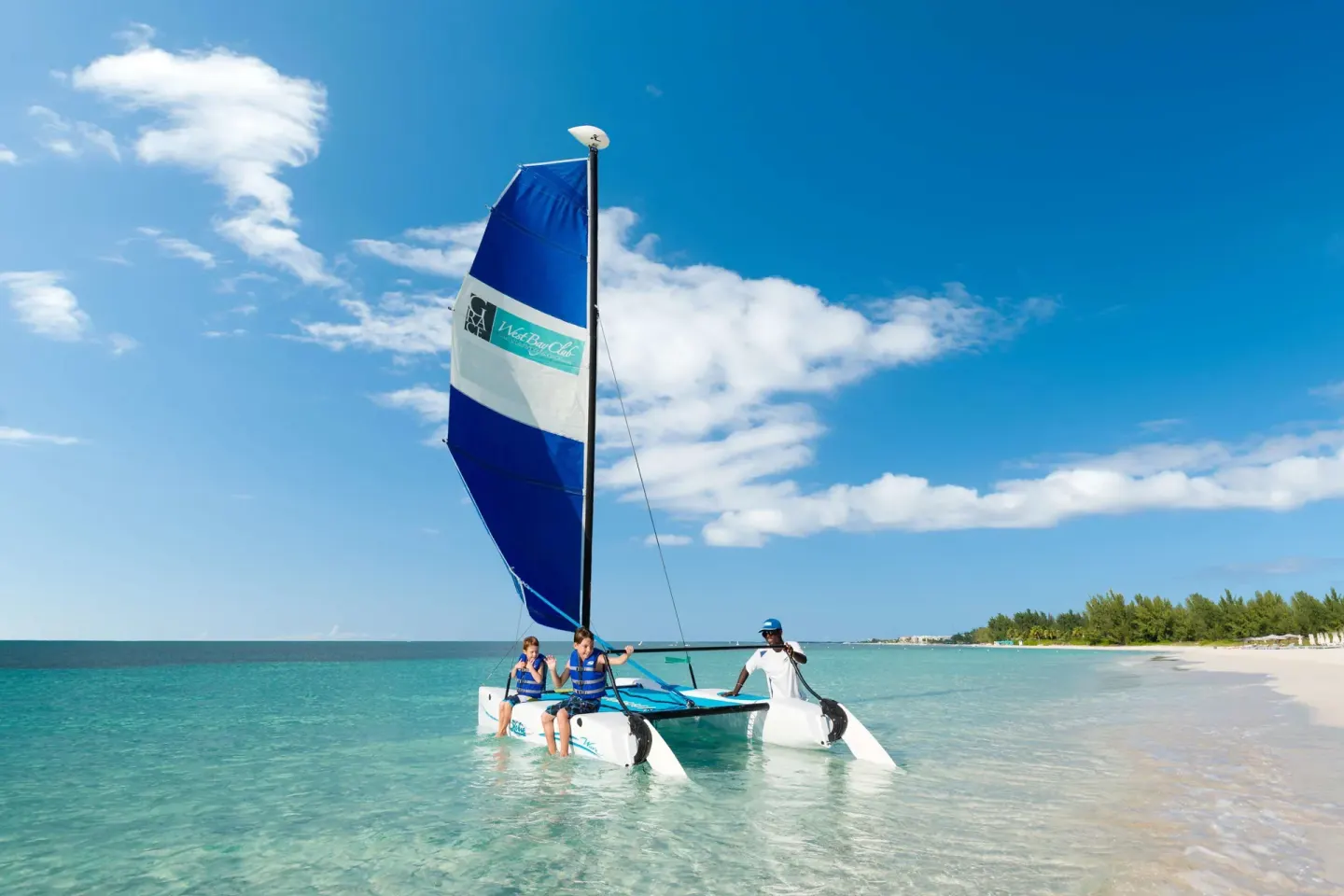 Guests sail a small catamaran in clear water off West Bay Club beach.