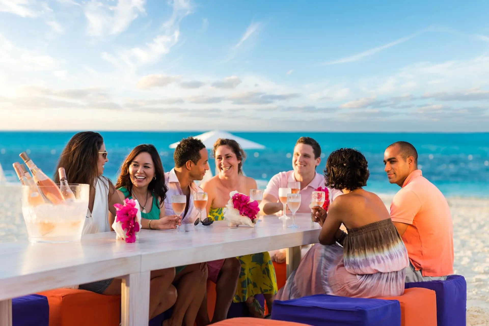 Guests share drinks at a beachfront table at West Bay Club with the ocean behind them.