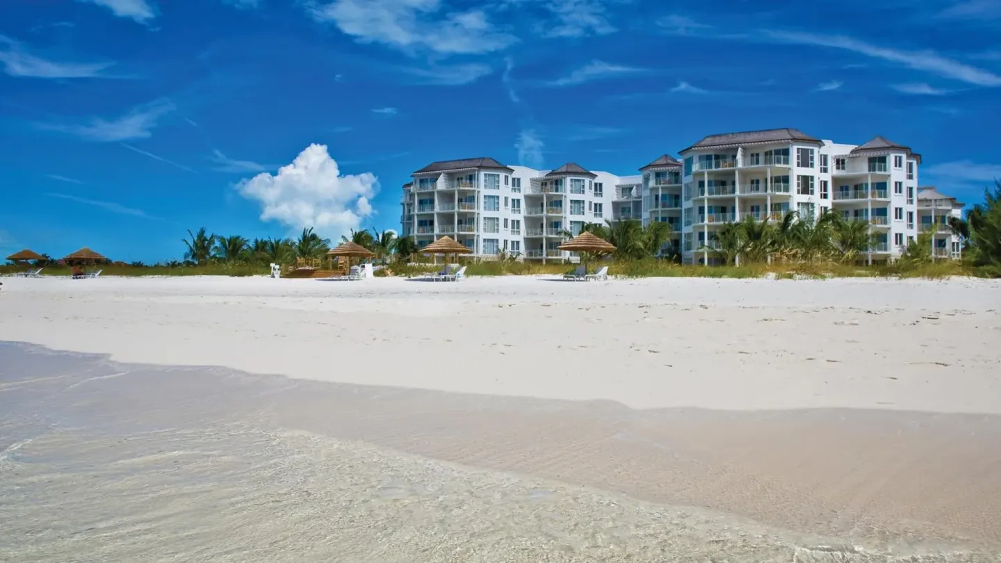 West Bay Club beachfront buildings seen from the shoreline with white sand in front.