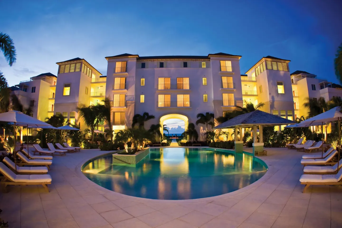 Evening pool courtyard with loungers and illuminated resort buildings at West Bay Club.