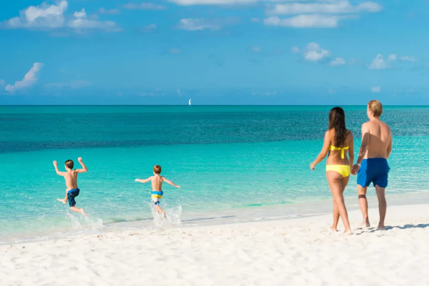 Family walking and children running into turquoise water at West Bay Club.