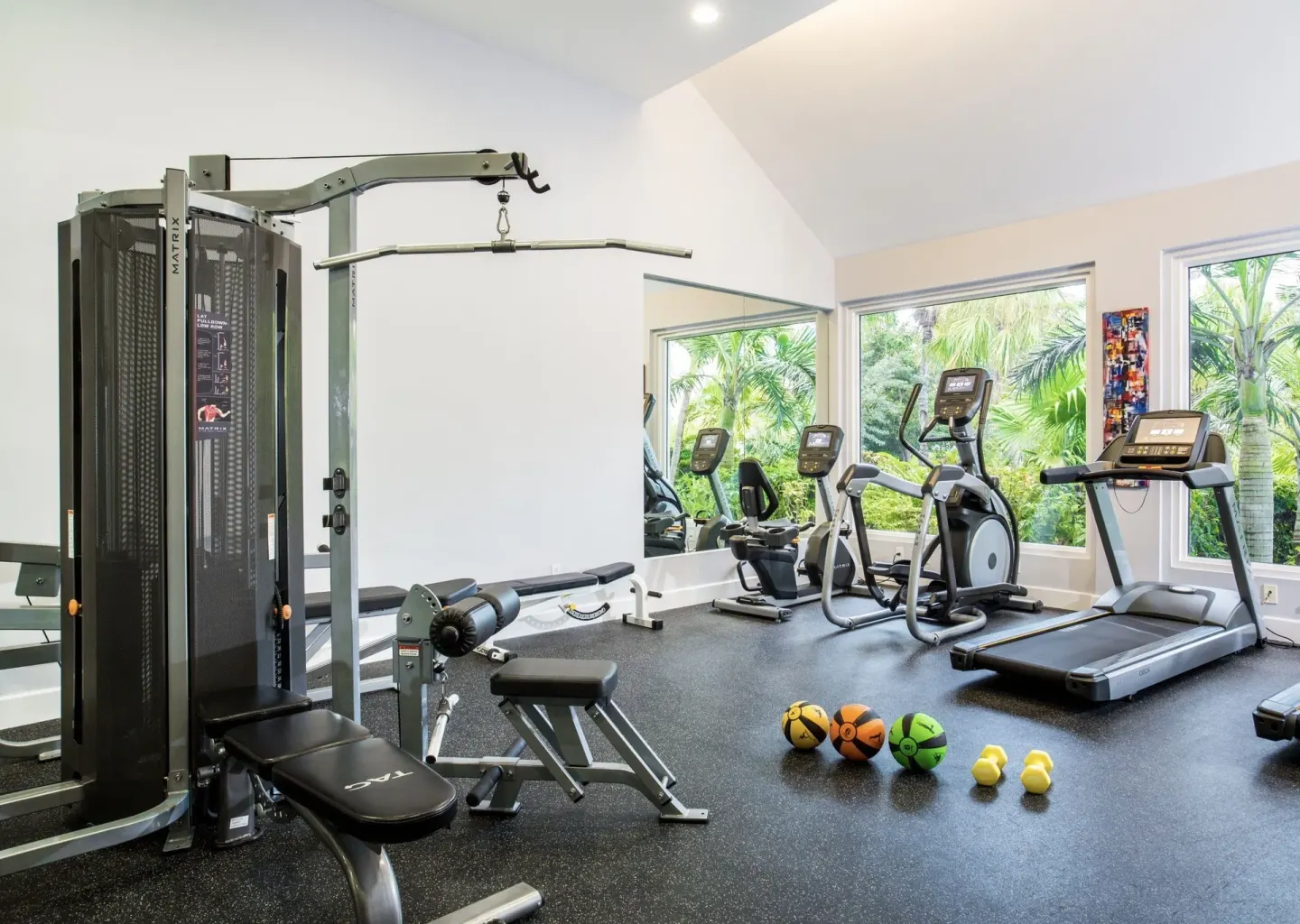 Fitness room with treadmills, cardio machines, weights, and windows at West Bay Club.