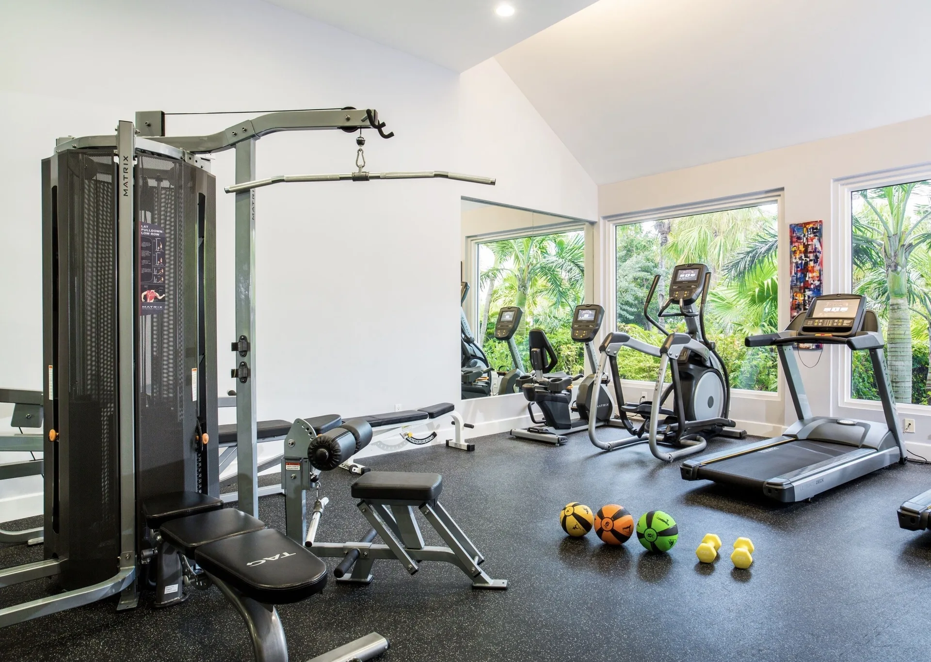 Fitness room with treadmills, cardio machines, weights, and windows at West Bay Club.
