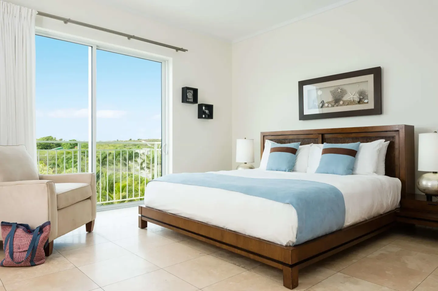 Guest bedroom with king bed, armchair, and balcony view at West Bay Club.