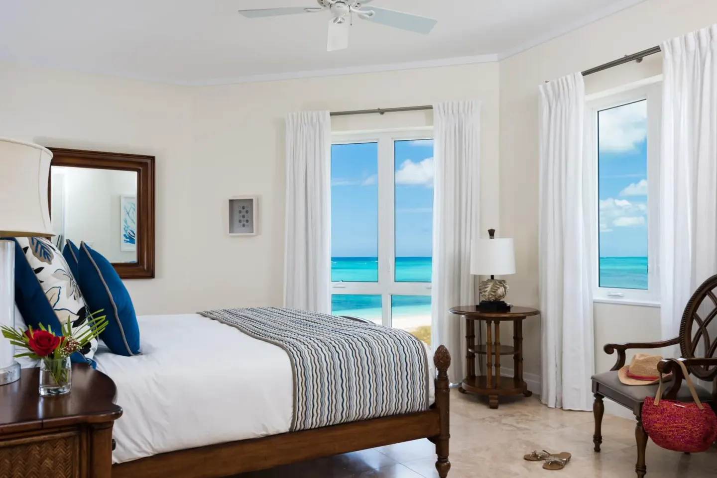 Ocean-view bedroom at West Bay Club with a wood bed, white curtains, and turquoise water beyond the windows.
