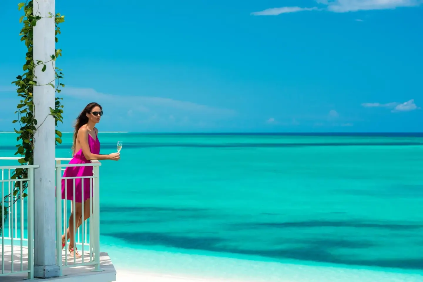 A guest stands on a white balcony above turquoise water at West Bay Club.