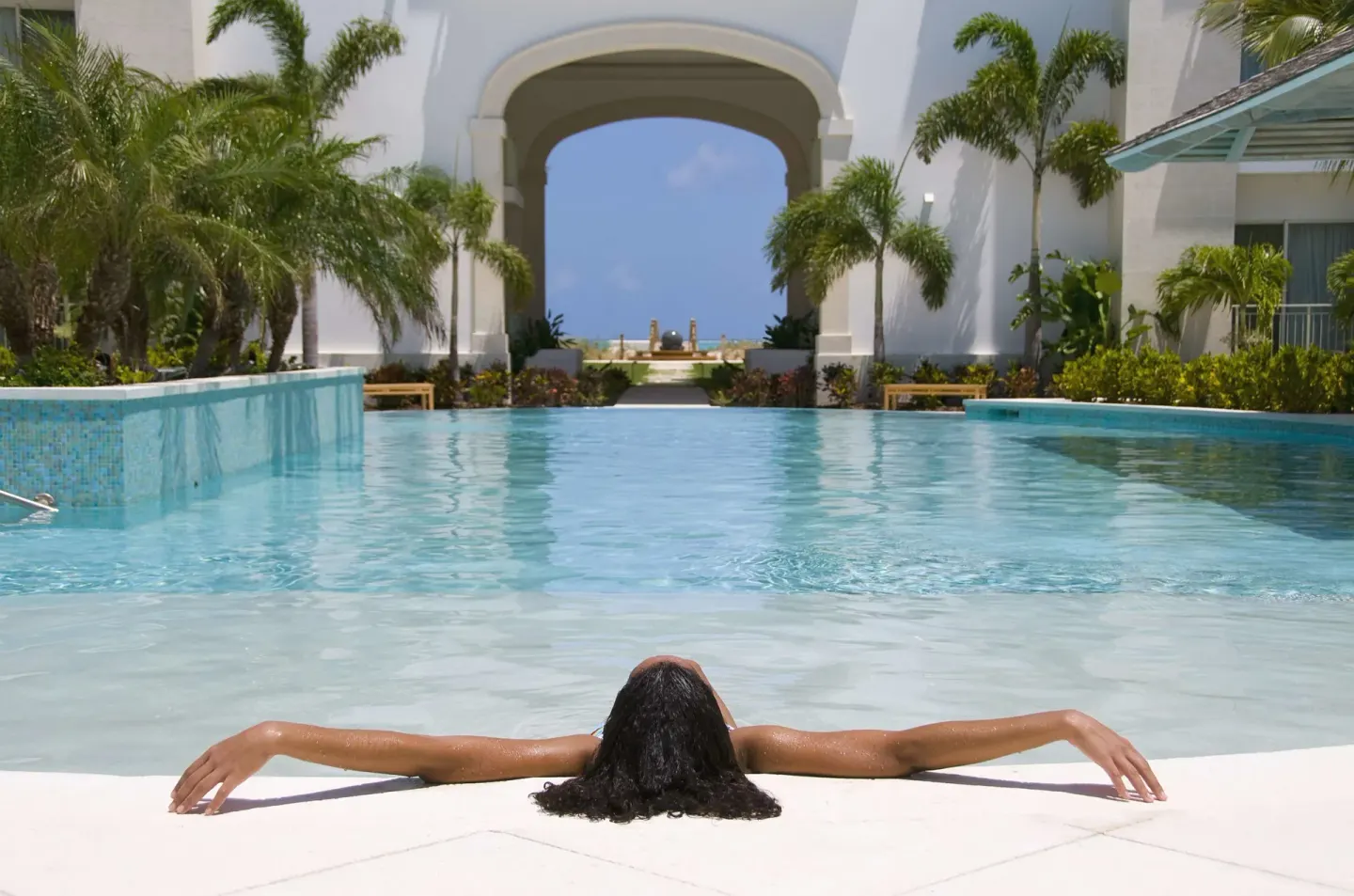 Guest relaxing in the pool courtyard with palms and an archway at West Bay Club.