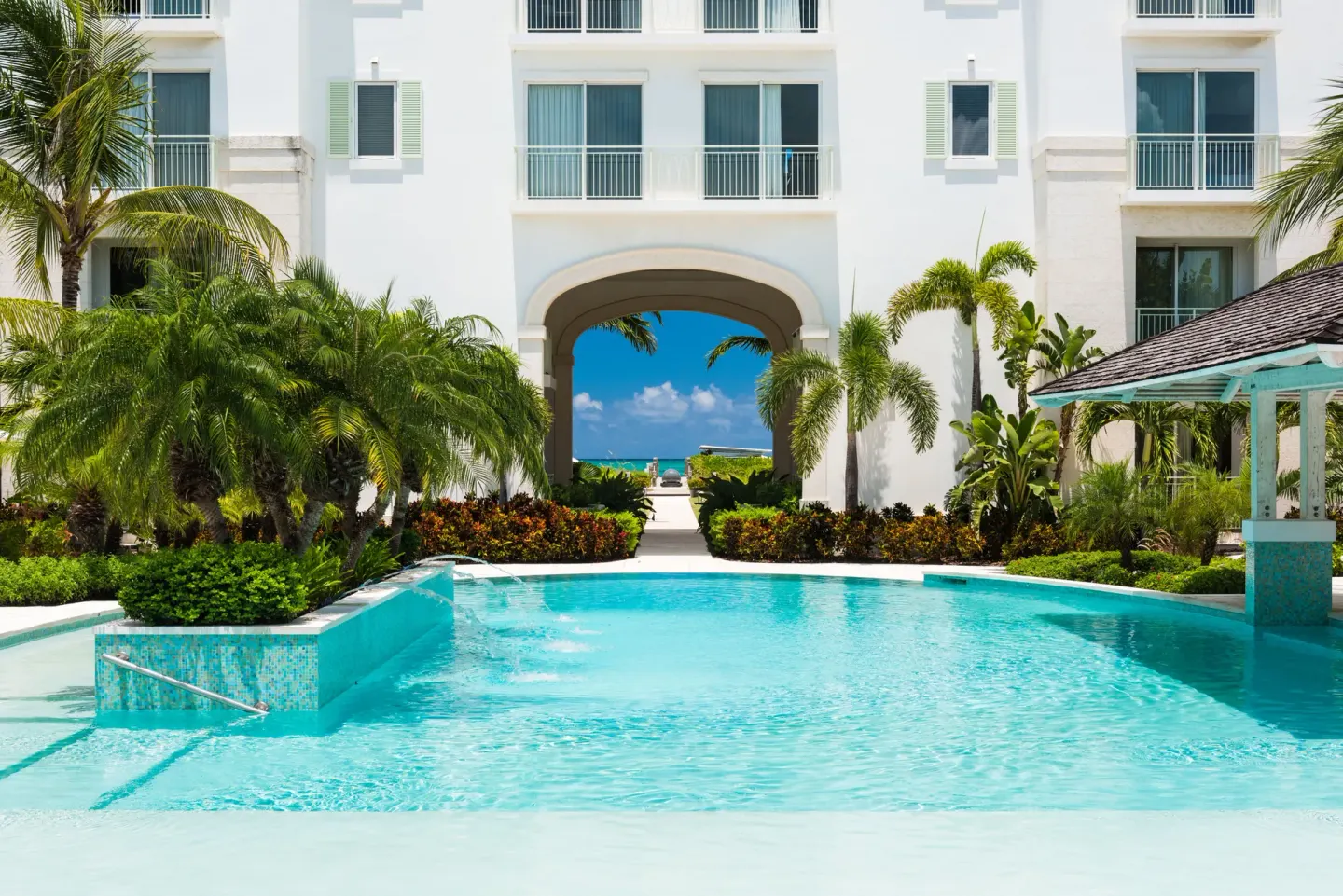 Resort pool with palms and an arched building view toward the ocean at West Bay Club.