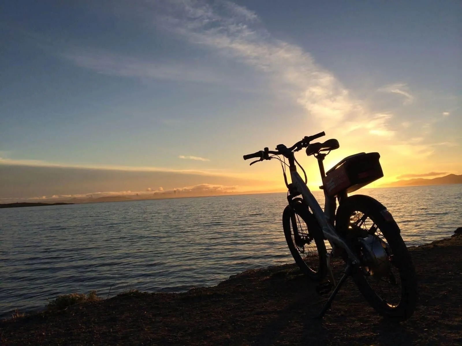 A bicycle is silhouetted beside the water at sunset near West Bay Club.