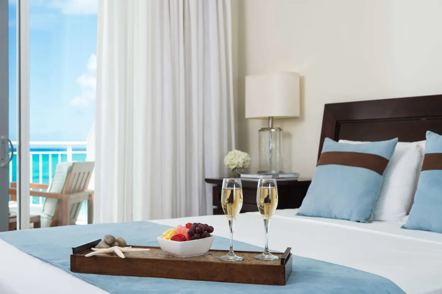 Oceanfront king bed in a Luxury Suite at West Bay Club with balcony and turquoise water beyond.