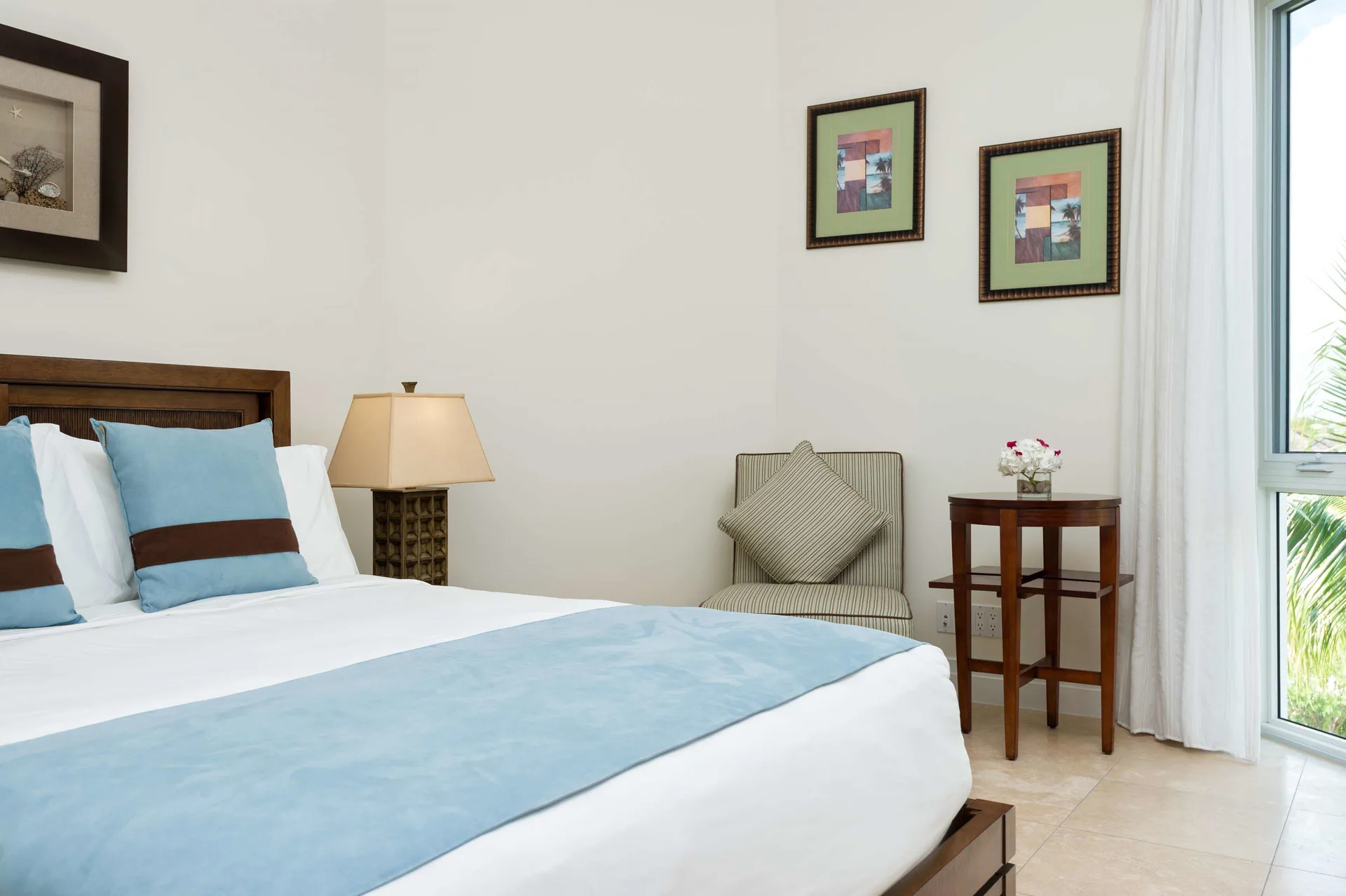 Studio Garden View room with king bed, blue accents, chair, and tall window at West Bay Club.