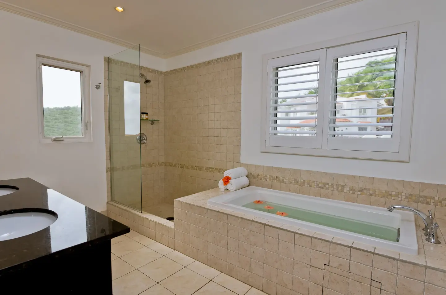 Bathroom with tiled soaking tub, glass shower, and shuttered window at Windjammer Landing Resort and Residences.