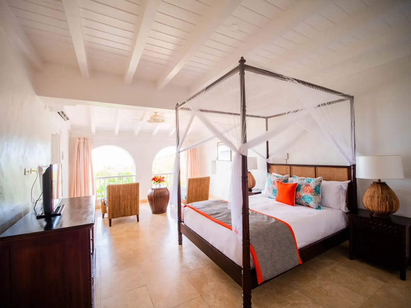 Four-poster guest room at Windjammer Landing Resort and Residences with sitting area and arched balcony doors.