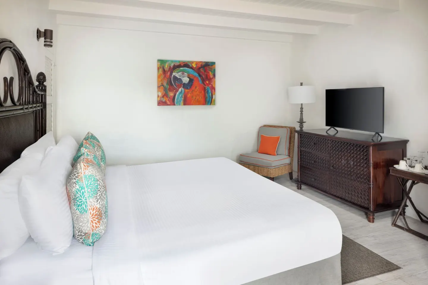 Guest room at Windjammer Landing Resort and Residences with white bed, parrot artwork, TV and carved dresser.