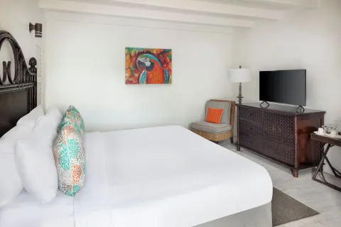 Guest room at Windjammer Landing Resort and Residences with white bed, parrot artwork, TV and carved dresser.