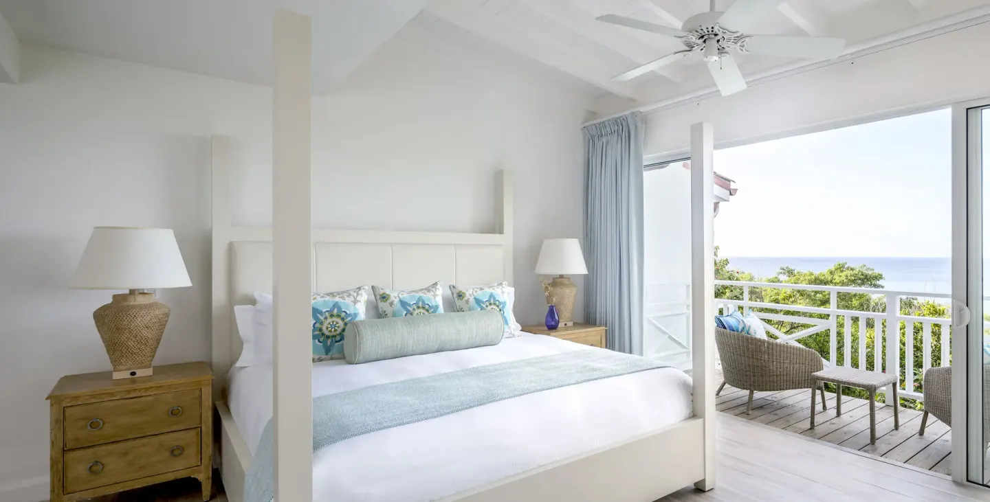 White four-poster king bed beside a balcony with ocean view at Windjammer Landing Resort and Residences.