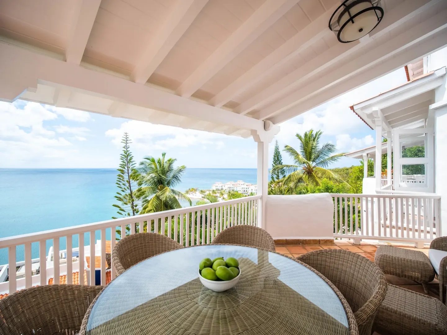 Covered hilltop villa terrace with wicker dining set and sea view at Windjammer Landing Resort and Residences.