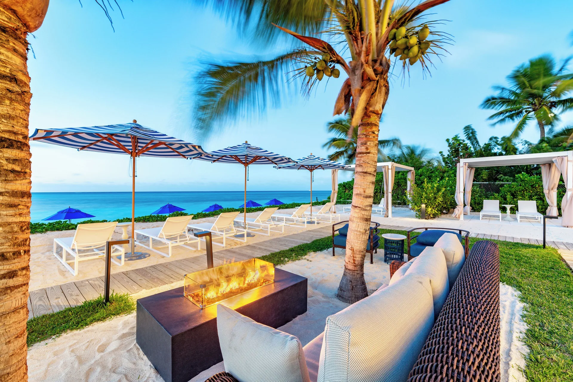 Beach lounge area with cabanas, umbrellas, and fire feature at Windsong on the Reef.