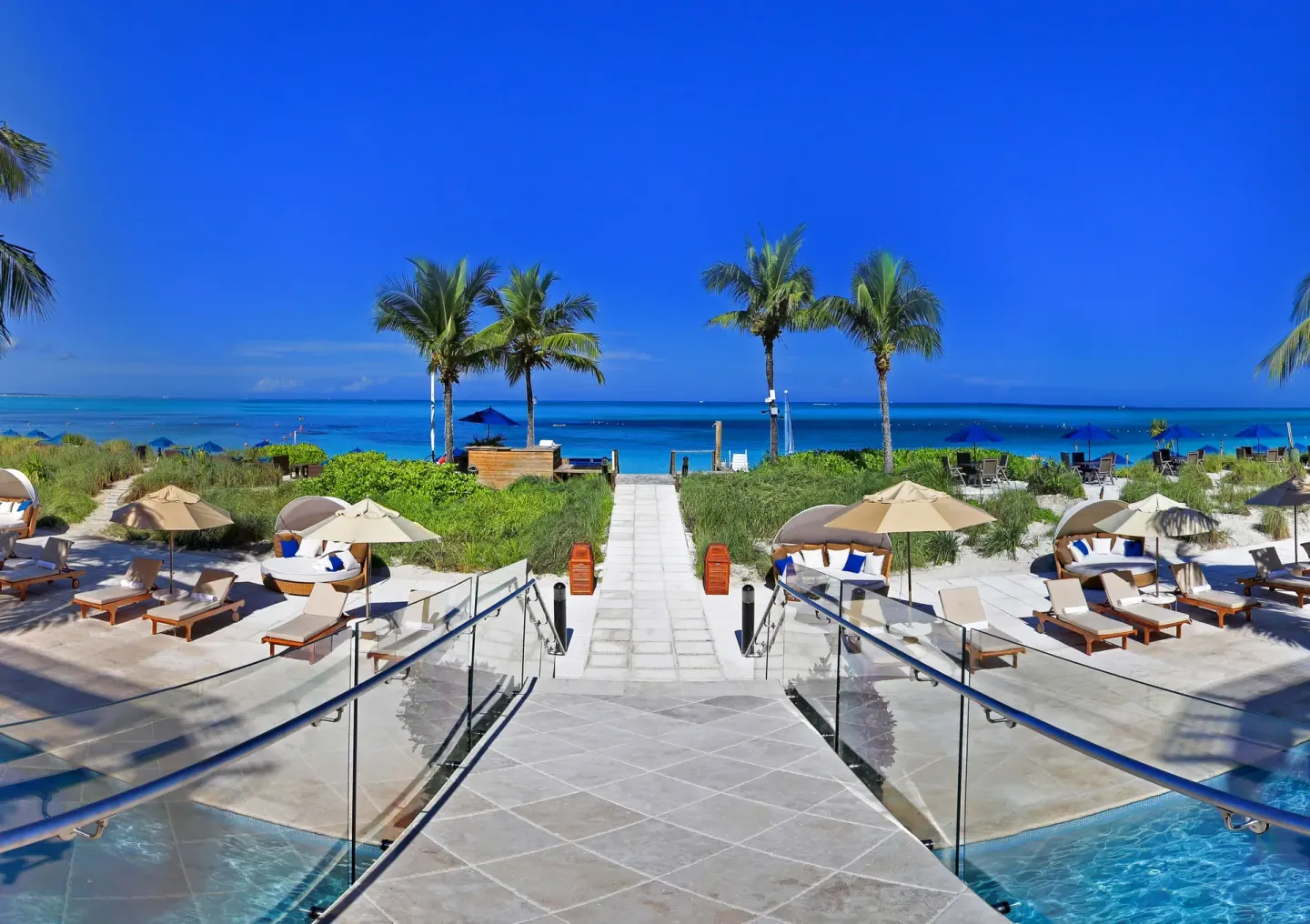 Beach walkway, lounge chairs, palms, and turquoise water at Windsong on the Reef.
