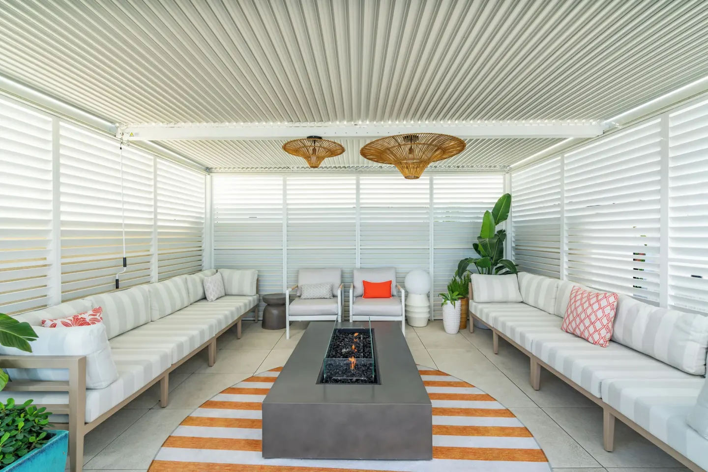 A covered lounge with sofas and a fire table is shown at Windsong on the Reef.