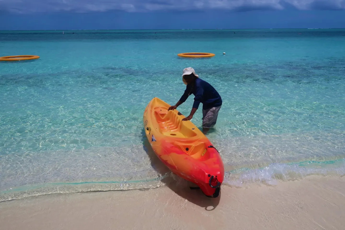 A staff member pulls an orange kayak into shallow water at Windsong on the Reef.