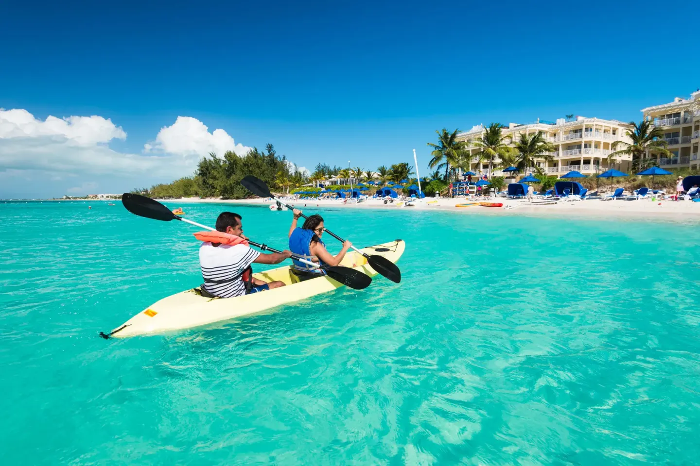 Two guests kayak in turquoise water off the beach at Windsong on the Reef.